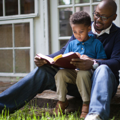 Pai e filho pequeno lendo a Bíblia sentados na varanda de casa