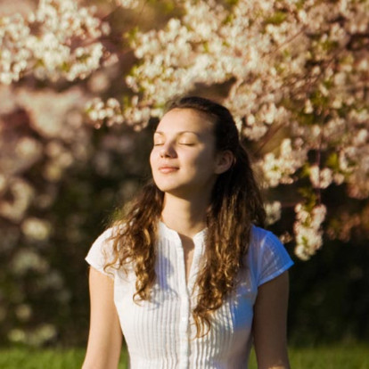 Mulher de olhos fechados, meditativa, com o rosto iluminado por luz solar suave em um bosque