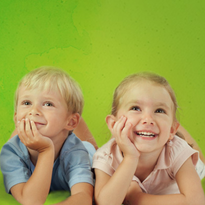 Duas crianças deitadas no chão e sorrindo para a câmera sobre um fundo verde